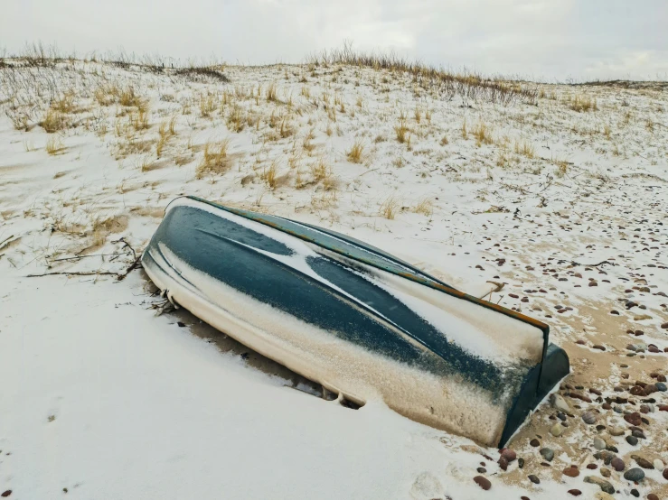 a boat sitting on top of a sandy beach, by Emma Andijewska, unsplash, land art, snow on the body, casket, upset, 90s photo