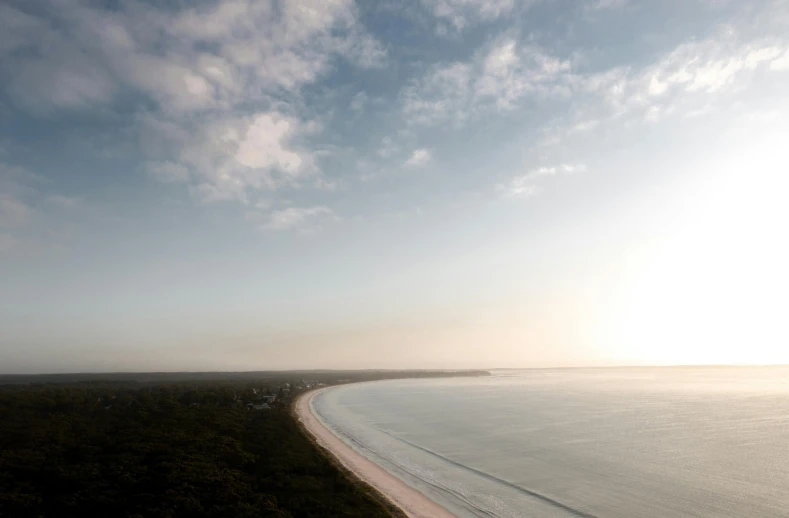 a person riding a surfboard on top of a sandy beach, by Peter Churcher, unsplash contest winner, minimalism, flying over the horizon, early morning lighting, australian beach, distant forest horizon