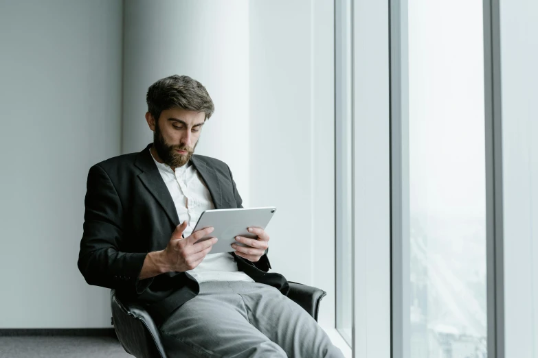 a man sitting in a chair looking at a tablet, trending on pexels, office clothes, bearded and built, avatar image, professional image