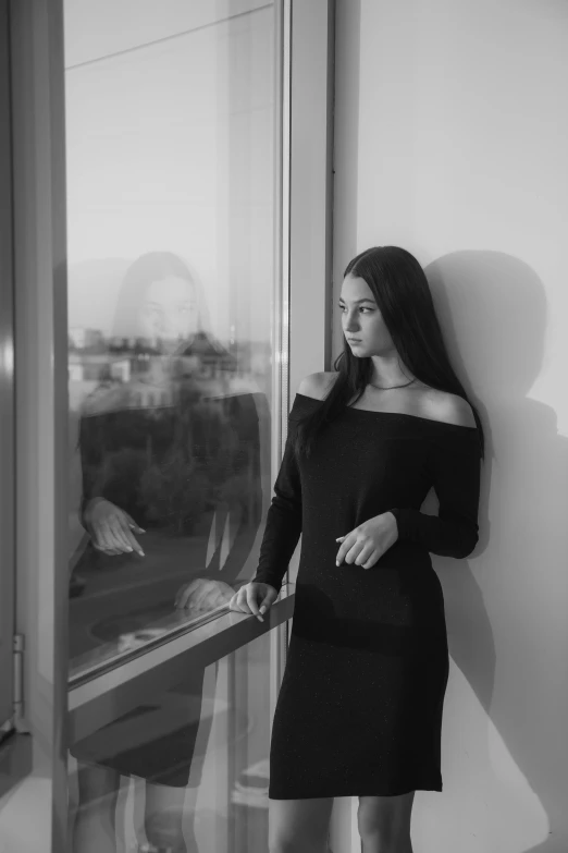 a black and white photo of a woman leaning against a window, by Dimitre Manassiev Mehandjiysky, young woman with long dark hair, dilraba dilmurat, wearing a black dress, window ( city )