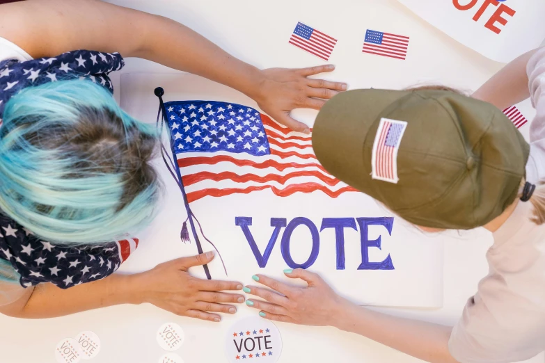 a group of people standing around a sign that says vote, a photo, trending on pexels, fourth of july, hand on table, college girls, avatar image