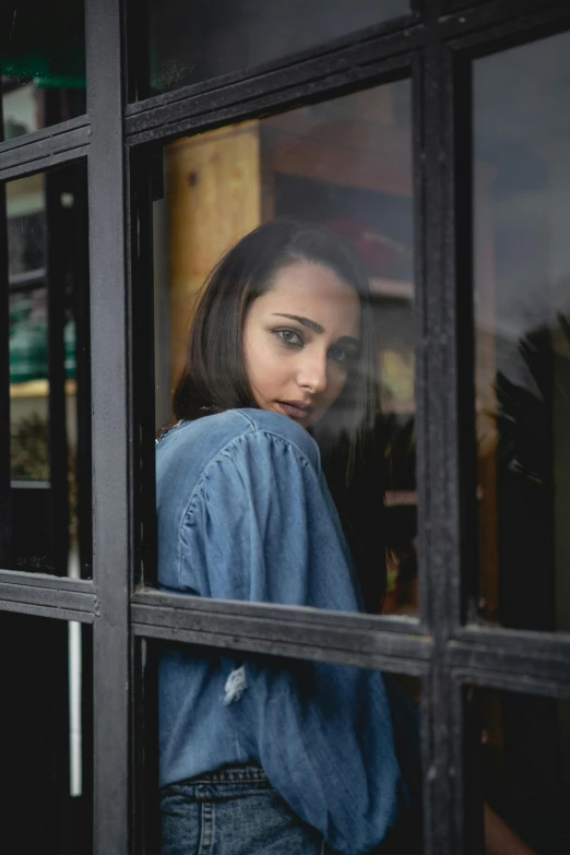 a woman is looking out of a window, pexels contest winner, realism, young middle eastern woman, casual pose, in doors, serious look