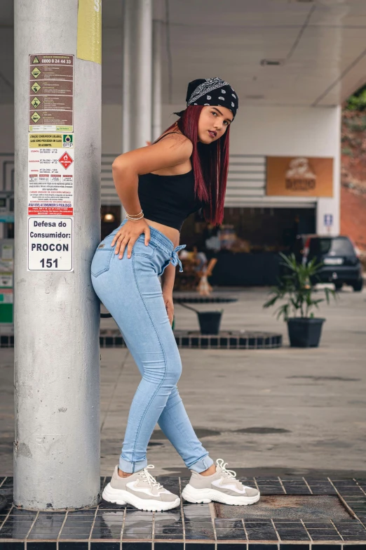 a woman in jeans and a bandana leaning against a pole, an album cover, by Alejandro Obregón, trending on pexels, woman in streetwear, redhead girl, latinas, breeches