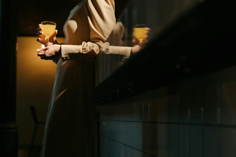 a woman standing in a kitchen holding a glass of wine, inspired by Georges de La Tour, unsplash, yellow robes, volumetric evening lights, long shot from the back, sleek robes