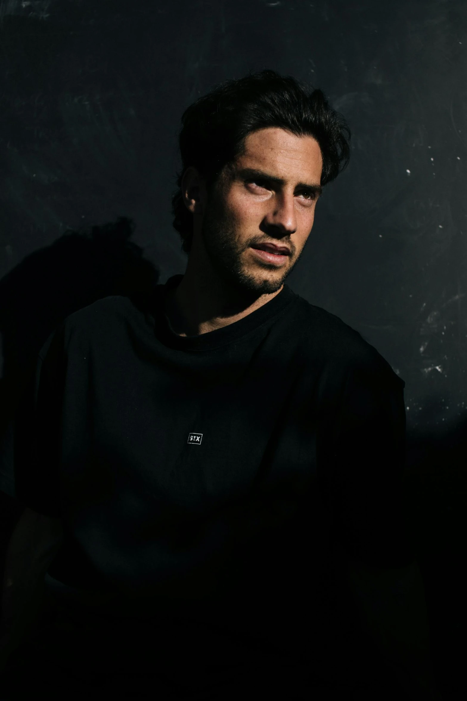 a man sitting in a chair in a dark room, wearing a black tshirt, orelsan, photo of a model, rugged face