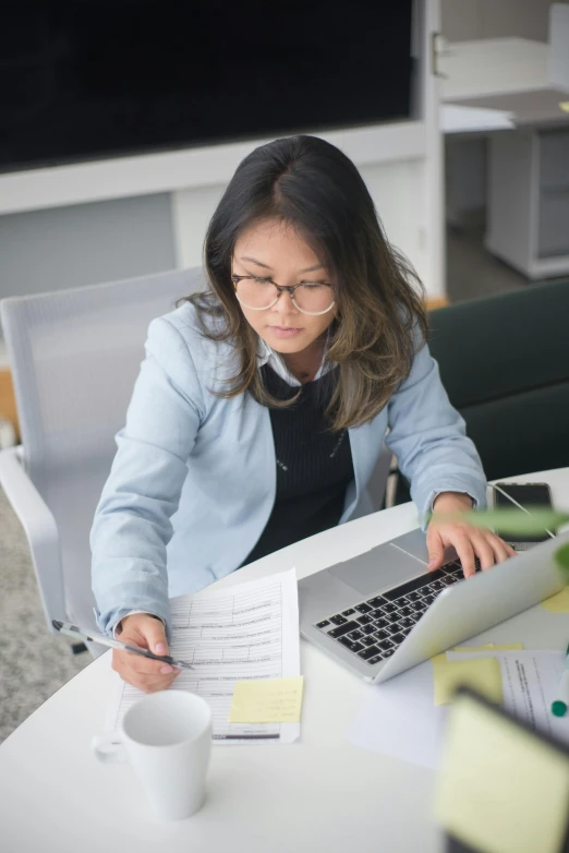 a woman sitting at a table working on a laptop, inspired by Li Di, pexels contest winner, female in office dress, asian female, gif, low quality photo