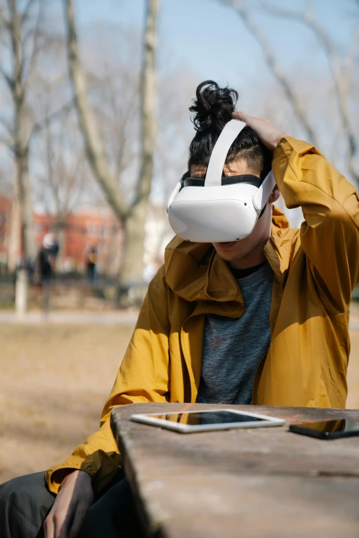 a person sitting at a table with a pair of headphones on, inspired by Feng Zhu, renaissance, vr glasses, at a park, 2019 trending photo, visor covering eyes