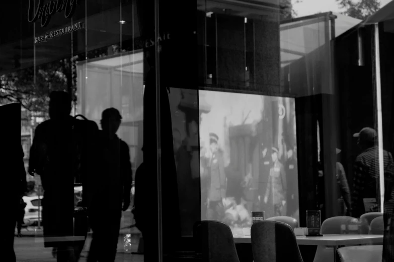 a group of people standing in front of a window, a black and white photo, inspired by Vivian Maier, photo of the cinema screen, man walking through city, reflections on a glass table, photo for a store