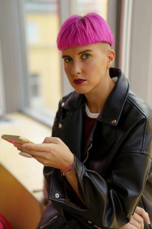 a woman with pink hair is looking at her cell phone, a portrait, by Julia Pishtar, trending on pexels, brown buzzcut, wearing leather jacket, nonbinary model, gold hair