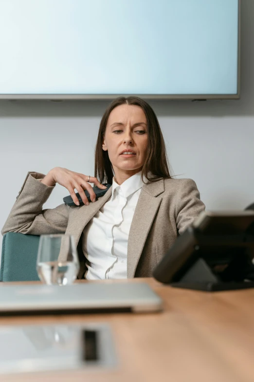 a woman sitting at a table in front of a laptop, wearing a worn out suit, trending photo, thumbnail, in a meeting room