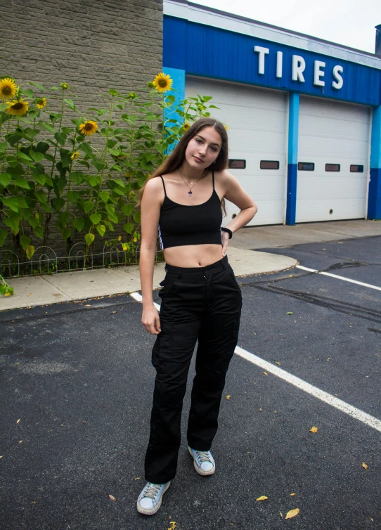 a woman standing in a parking lot next to a building, baggy black pants, kailee mandel, wearing a crop top, subreddit / r / whale