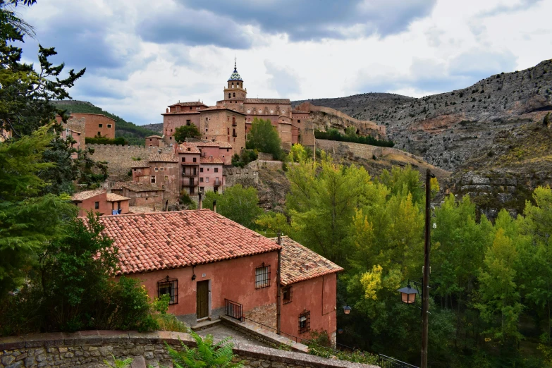 a red building sitting on top of a lush green hillside, inspired by Luis Paret y Alcazar, pexels contest winner, romanesque, square, view of villages, gray, spanish