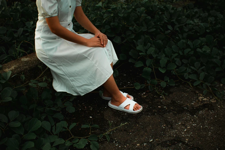 a woman in a white dress sitting on a rock, inspired by Elsa Bleda, pexels contest winner, birkenstock sandals, walking at the garden, white uniform, old school