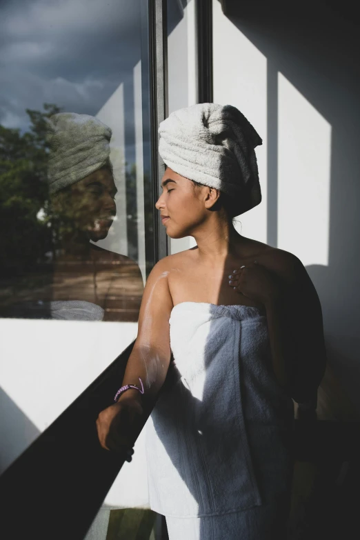 a woman standing by a window with a towel on her head, by Lily Delissa Joseph, unsplash, happening, beautiful tan mexican woman, sun behind him, lush surroundings, in bathroom