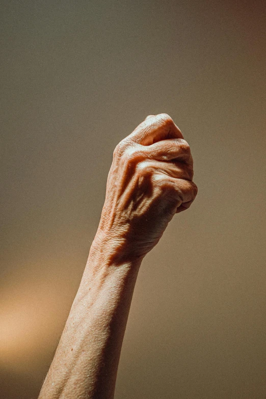 a close up of a person's arm with a light in the background, trending on pexels, raised fist, an elderly, detailed veiny muscles, plain background