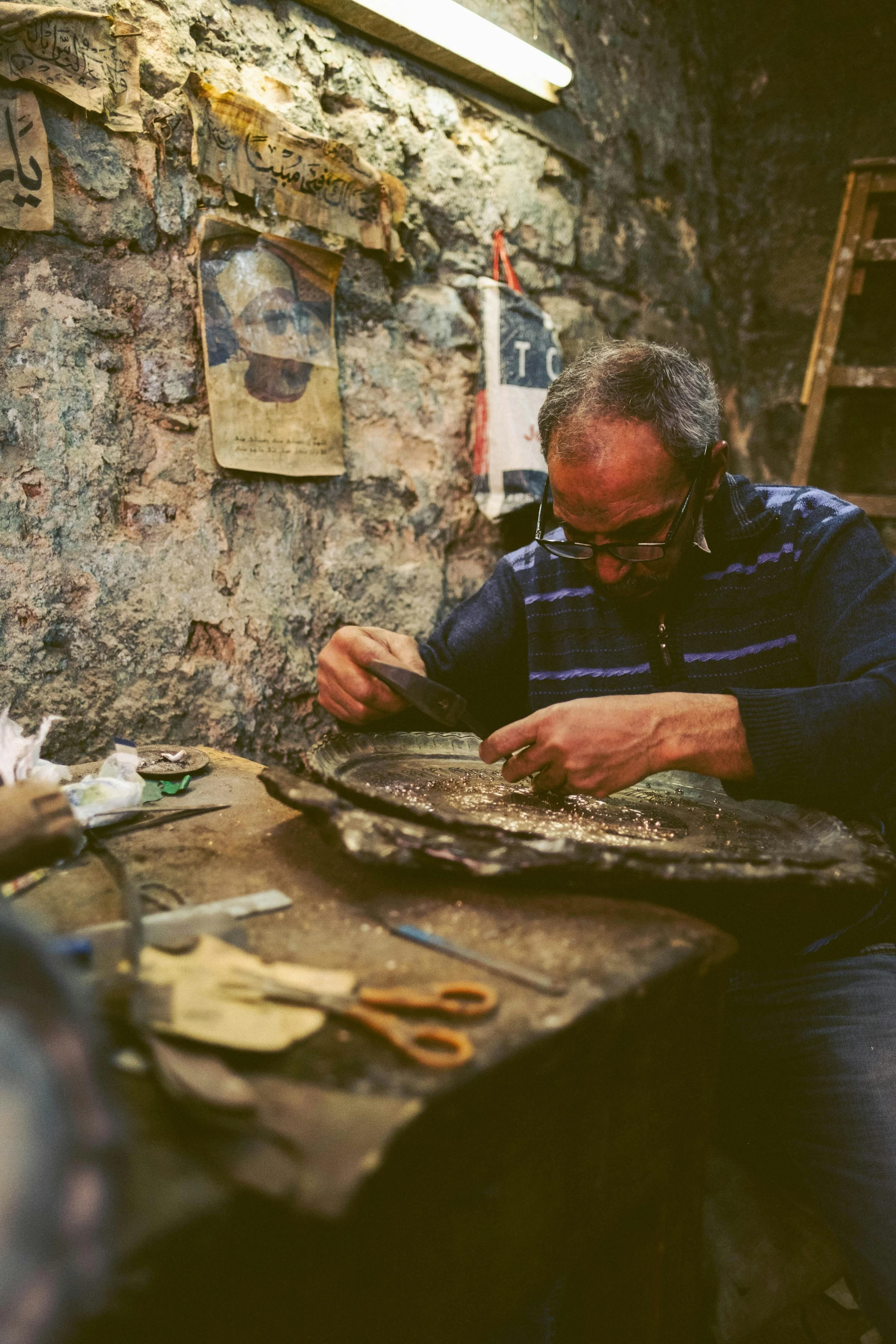 a man sitting at a table working on something, an album cover, pexels contest winner, arte povera, found in a cave made of clay, paua shell, stitching, restoration