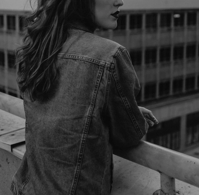 a black and white photo of a woman on a balcony, a black and white photo, pexels, realism, denim jacket, girl with brown hair, portait photo profile picture, lowres