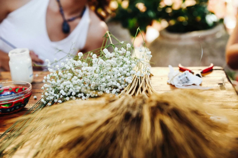 a woman sitting at a table with a bunch of flowers, by Lucia Peka, pexels contest winner, process art, cat tail, gypsophila, filling the frame, natural materials