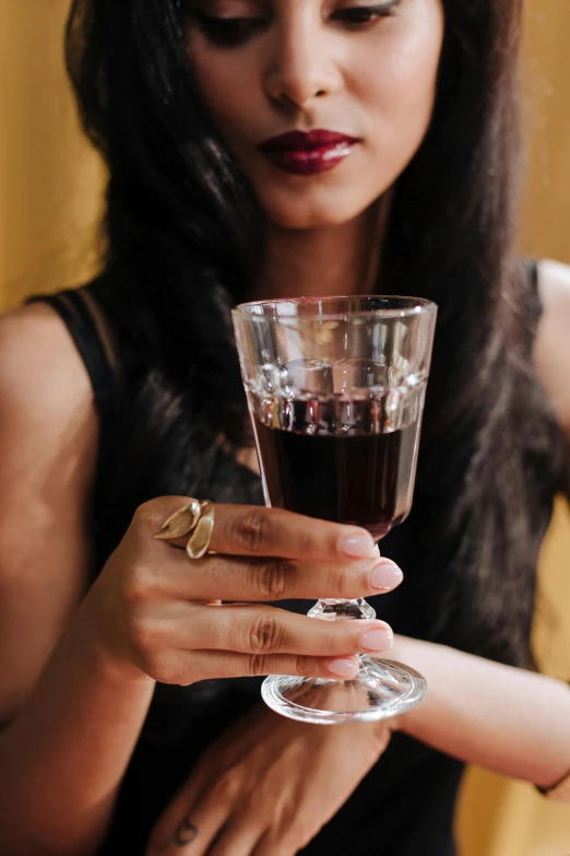 a woman in a black dress holding a glass of wine, by Julia Pishtar, trending on pexels, renaissance, dark-skinned, partially cupping her hands, instagram post, garnet