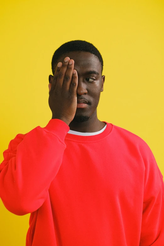 a man in a red sweatshirt covers his face with his hands, an album cover, by Stokely Webster, trending on pexels, yellow eye, yasuke 5 0 0 px models, virgil abloh, smooth background