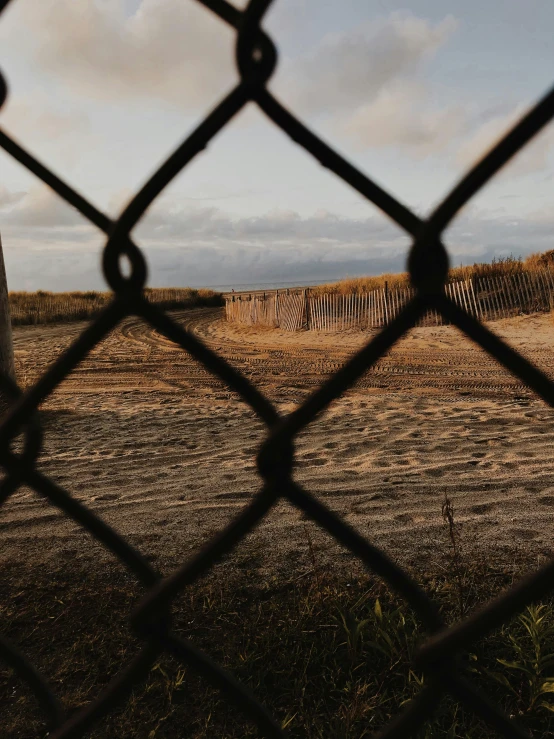 a fence that is next to a dirt field, by Ryan Pancoast, unsplash, overlooking the beach, behind bars, low quality photo, dimly lit