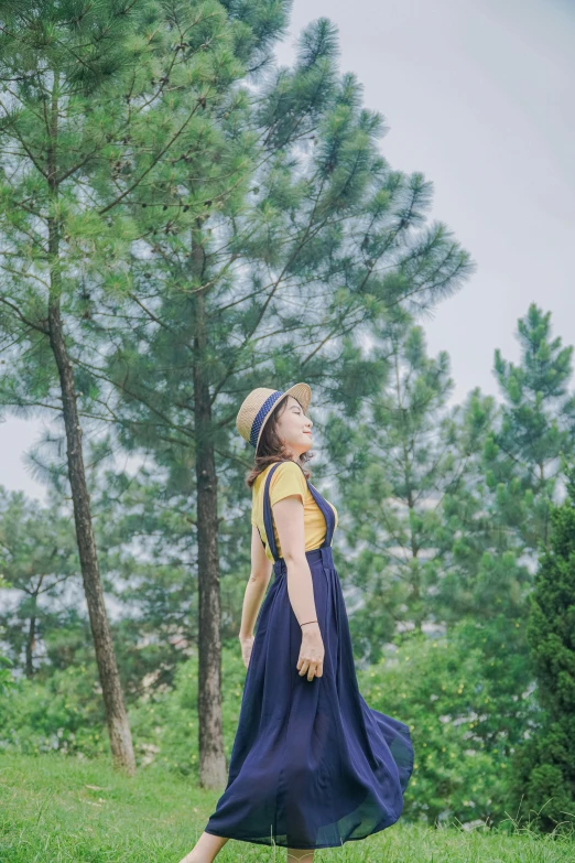 a woman standing on top of a lush green field, a picture, inspired by Oleg Oprisco, unsplash, pine trees in the background, girl wearing uniform, blue and yellow theme, profile image