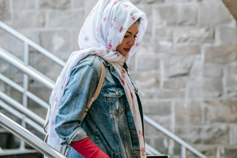 a woman in a hijab is walking down the stairs, trending on pexels, hurufiyya, wearing a jeans jackets, white and pink cloth, he‘s wearing a red scarf, patterned clothing