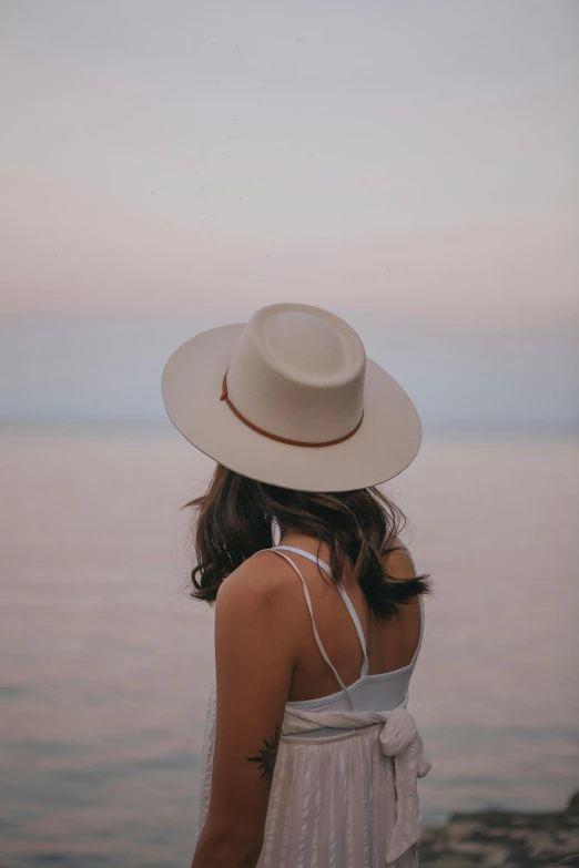 a woman wearing a hat looking out at the ocean, trending on pexels, soft evening lighting, white cowboy hat, girl with brown hair, with a sleek spoiler