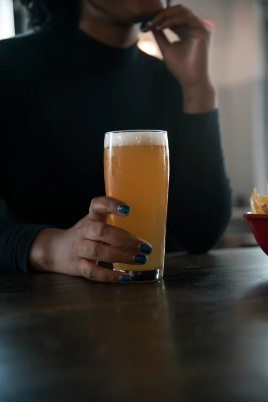 a woman sitting at a table with a glass of beer, by Carey Morris, pexels, closeup of arms, shot from cinematic, hop cone juice, buzzed sides