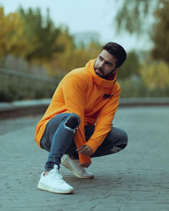 a man squatting down in the middle of a road, an album cover, inspired by Manjit Bawa, pexels contest winner, long orange sweatshirt, attractive pose, (((yellow))), gif