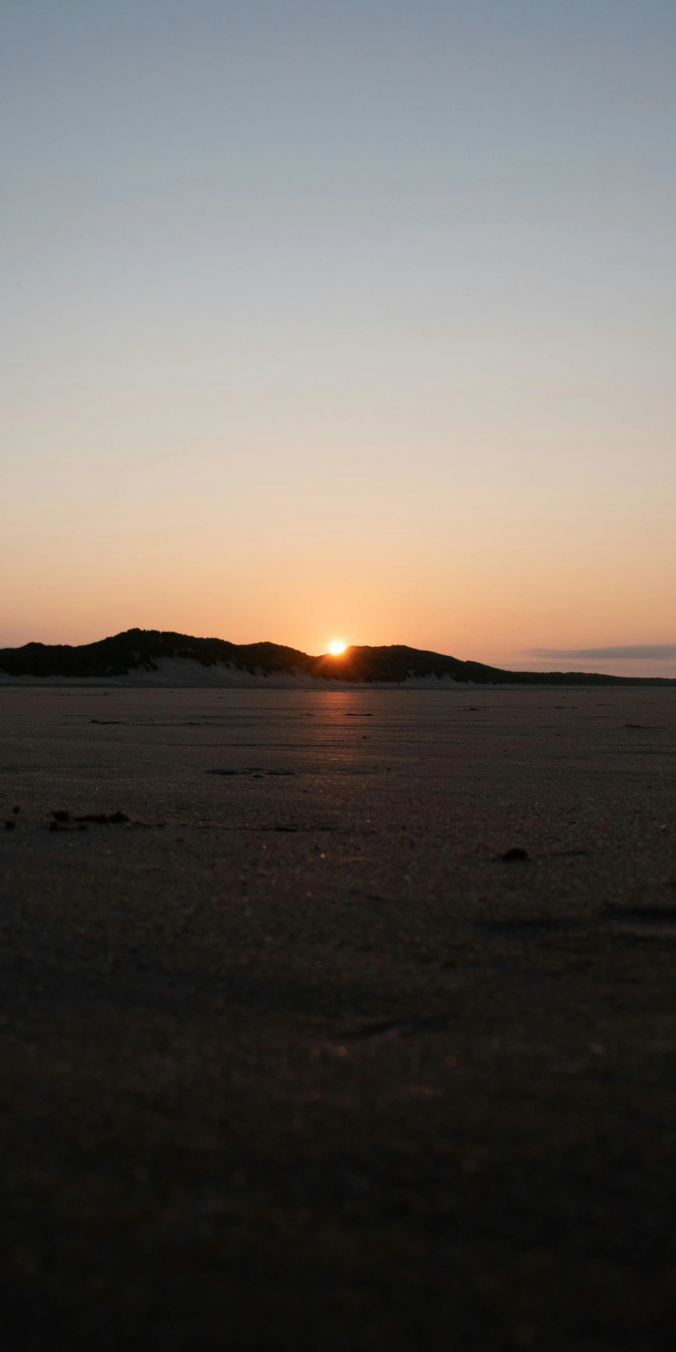 a man flying a kite on top of a sandy beach, a picture, by Elizabeth Durack, land art, sunset panorama, graafland, uploaded, distant - mid - shot