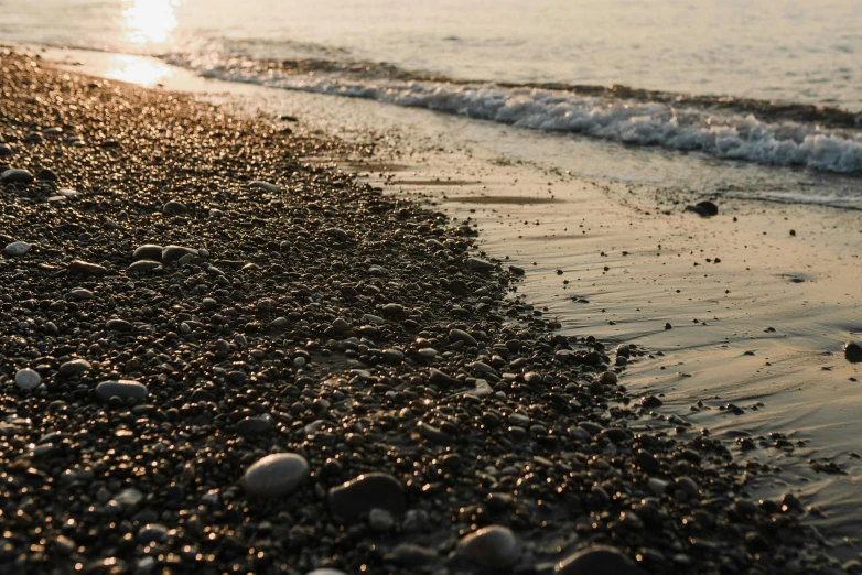 a person walking on a beach next to the ocean, pexels contest winner, gravels around, late afternoon sun, black sea, close-up photo