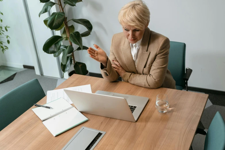 a woman sitting at a table in front of a laptop, post appocalyptic, a blond, facing to audience, high quality photo