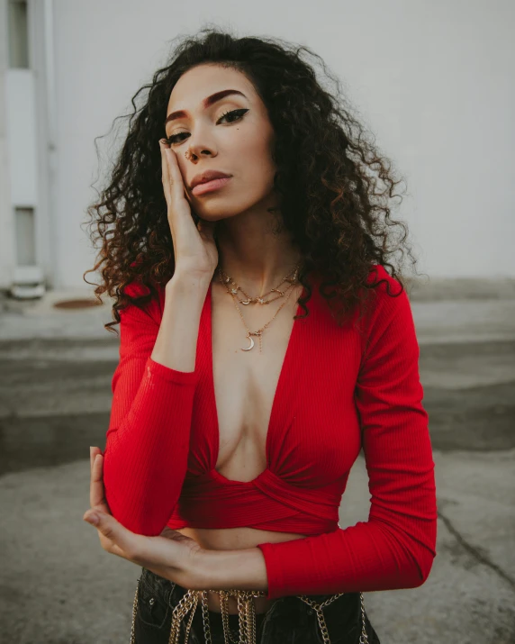 a woman in a red top posing for a picture, an album cover, trending on pexels, decolletage, light skin, queer woman, curls