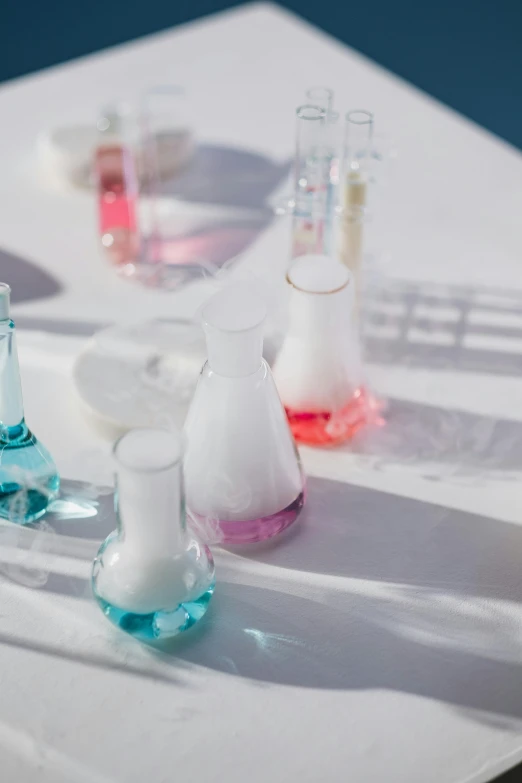 a group of vases sitting on top of a white table, a colorized photo, unsplash, with a lab coat, potions, on the ocean, blue and pink