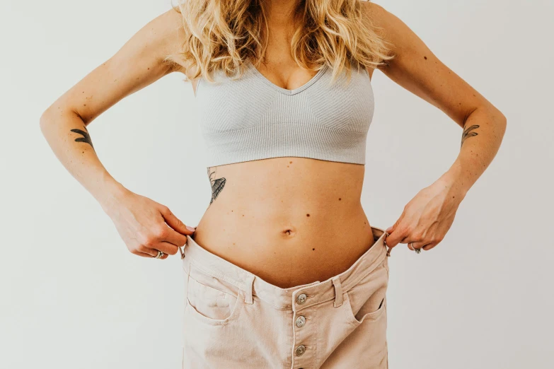 a woman standing with her hands in her pockets, by Nicolette Macnamara, trending on pexels, happening, belly button showing, scales covering her chest, ellie victoria gale, third trimester