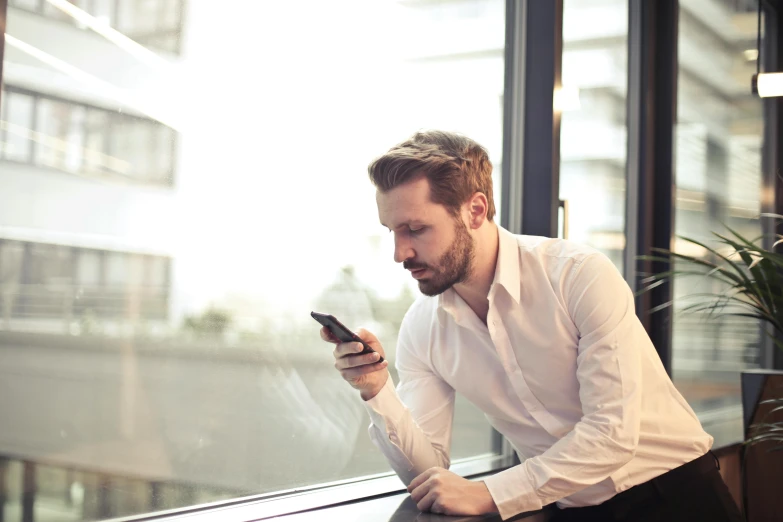 a man sitting on a window sill looking at his cell phone, pexels, blond brown stubble thin beard, corporate phone app icon, people at work, a single
