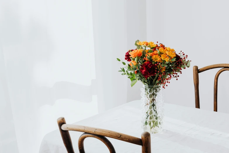 a vase filled with flowers sitting on top of a table, unsplash, on a white table, marigold, soft grey and red natural light, seated at a table