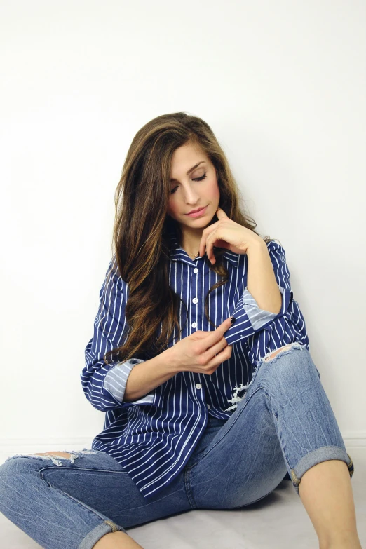 a woman sitting on the floor looking at her cell phone, an album cover, inspired by Eleanor Best, trending on pexels, wearing stripe shirt, thoughtful pose, pretty long hair, ( ( ( wearing jeans ) ) )