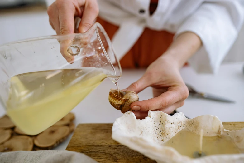 a close up of a person pouring something into a bowl, by Julia Pishtar, unsplash, shells and barnacles, dressed as a pastry chef, olive oil, marbling