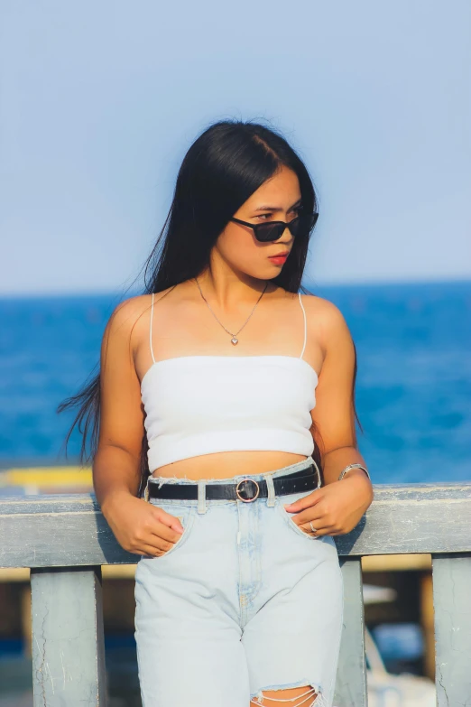 a woman sitting on a bench next to the ocean, by Robbie Trevino, croptop, avatar image, belt, asian