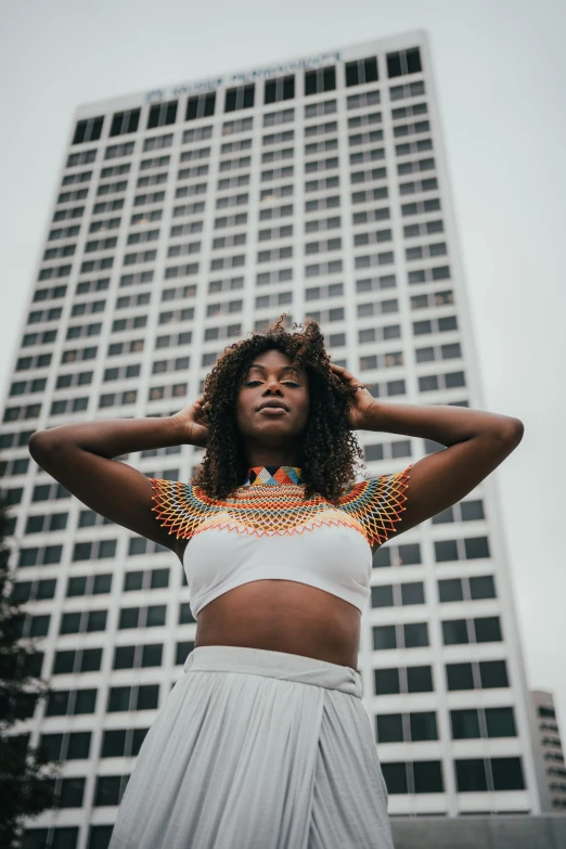 a woman standing in front of a tall building, trending on unsplash, afrofuturism, wearing a crop top, hands in her hair, varying ethnicities, white and black clothing