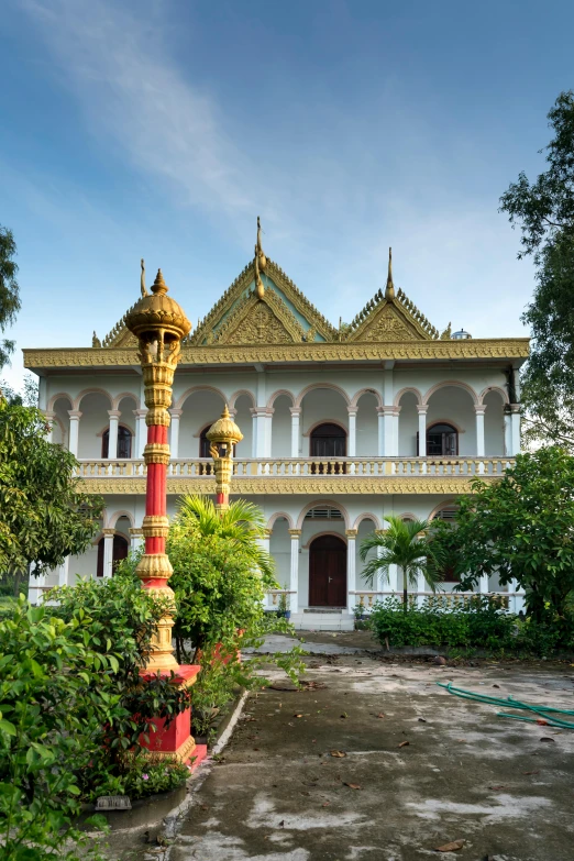 a red and gold lamp post in front of a building, cambodia, lush garden surroundings, minarets, raden saleh