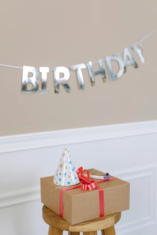 a gift box sitting on top of a wooden stool, a picture, bubble letters, made out of shiny silver, at a birthday party, detailed product image