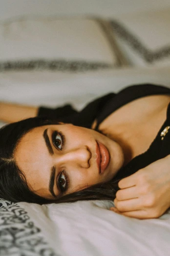 a beautiful young woman laying on top of a bed, by Julia Pishtar, trending on pexels, hurufiyya, middle eastern skin, straight eyebrows, black, low quality photo