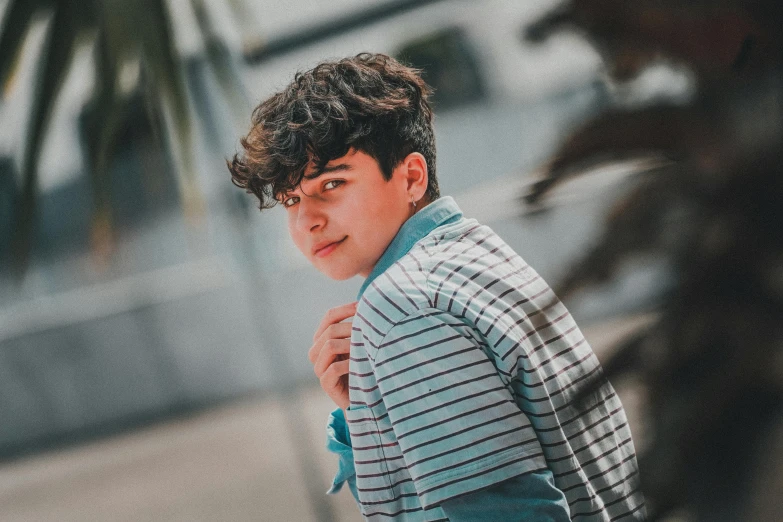 a young man standing in front of a palm tree, inspired by John Luke, pexels contest winner, renaissance, curly and short top hair, wearing stripe shirt, profile image, asher duran