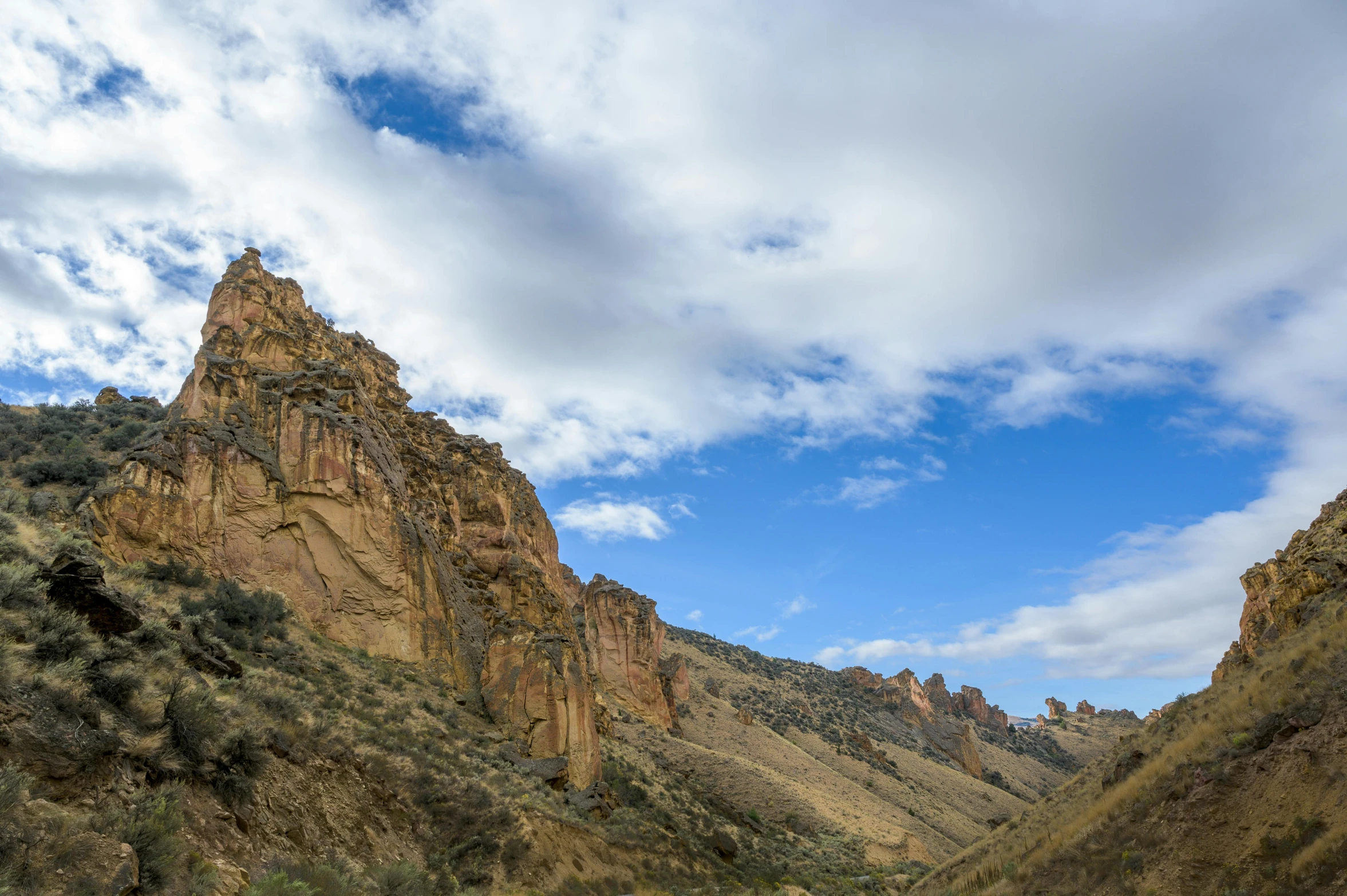 a man riding a motorcycle down a dirt road, unsplash, les nabis, tall stone spires, black mesa, panorama, ceremonial clouds