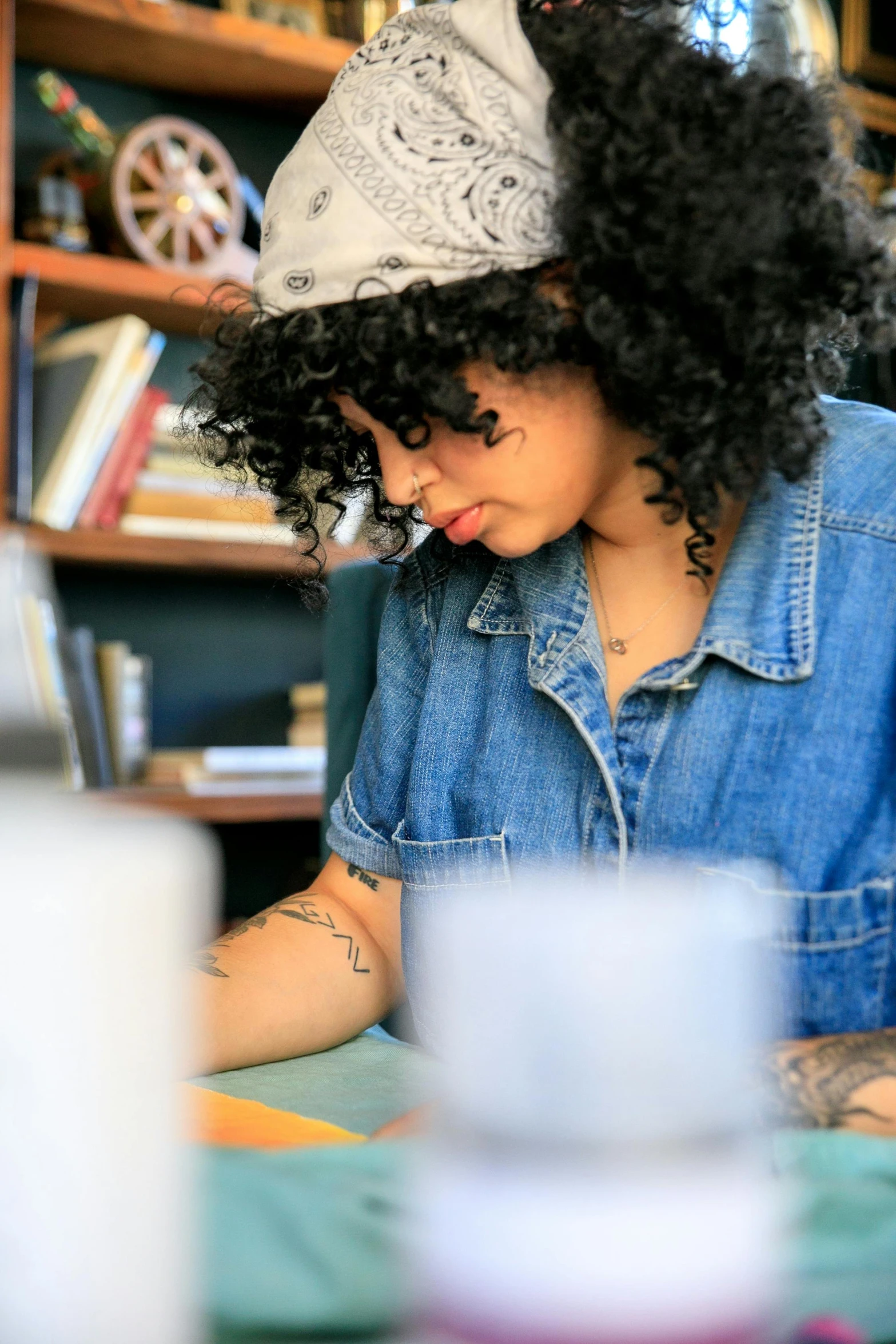 a woman sitting at a table working on a piece of art, pexels contest winner, academic art, curly afro, reading in library, photograph of a sleeve tattoo, handsome girl