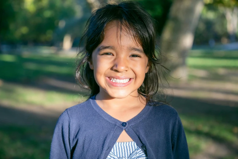 a young girl smiling at the camera in a park, by Gwen Barnard, pexels contest winner, hurufiyya, aboriginal, full daylight, screensaver, medium portrait top light