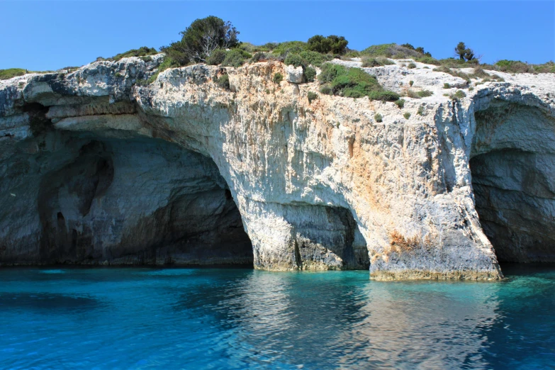 a large rock formation in the middle of a body of water, greek nose, light blue water, overgrown cave, marble walls